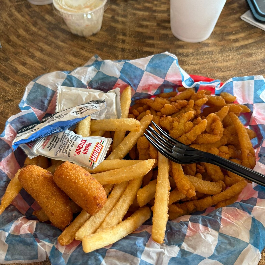 A basket of fried clam strips, corn nuggets and crinkle fries on checkered paper