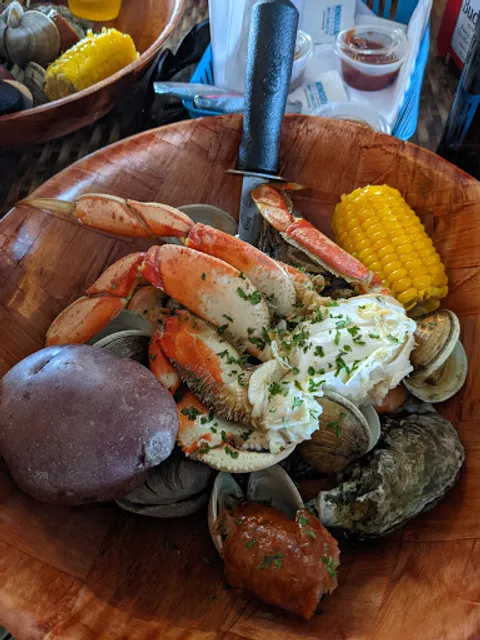 A wooden bowl of snow crab legs, clams, oysters, corn and potato with drawn butter